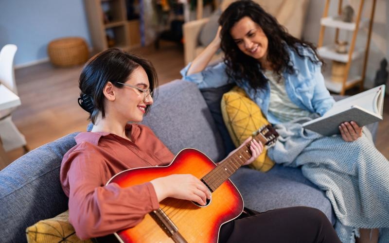 a person playing a guitar next to a person sitting on a couch